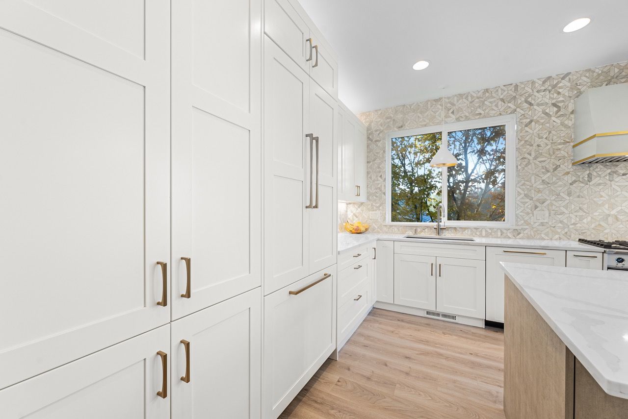 A kitchen with white cabinets and wooden floors and a large window.