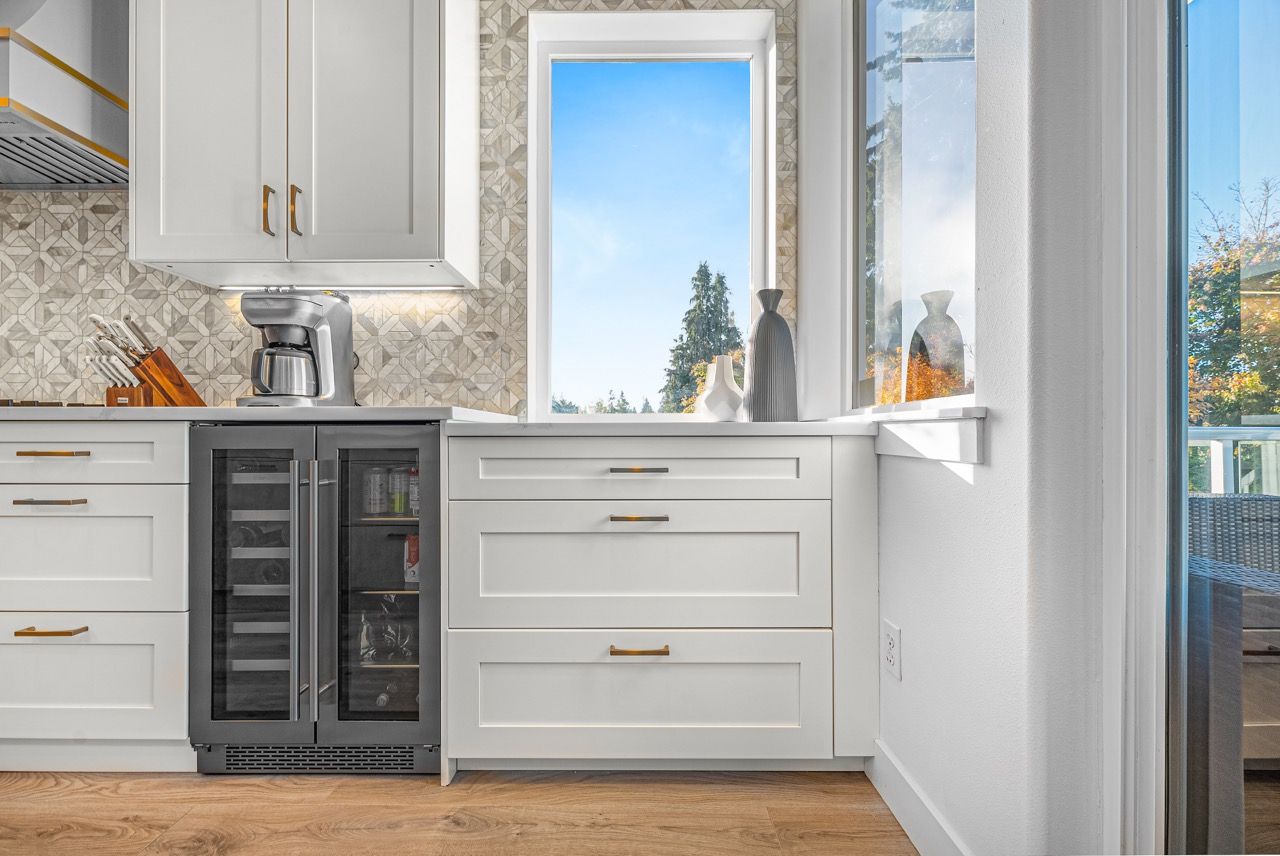 A kitchen with white cabinets , a wine cooler and a window.