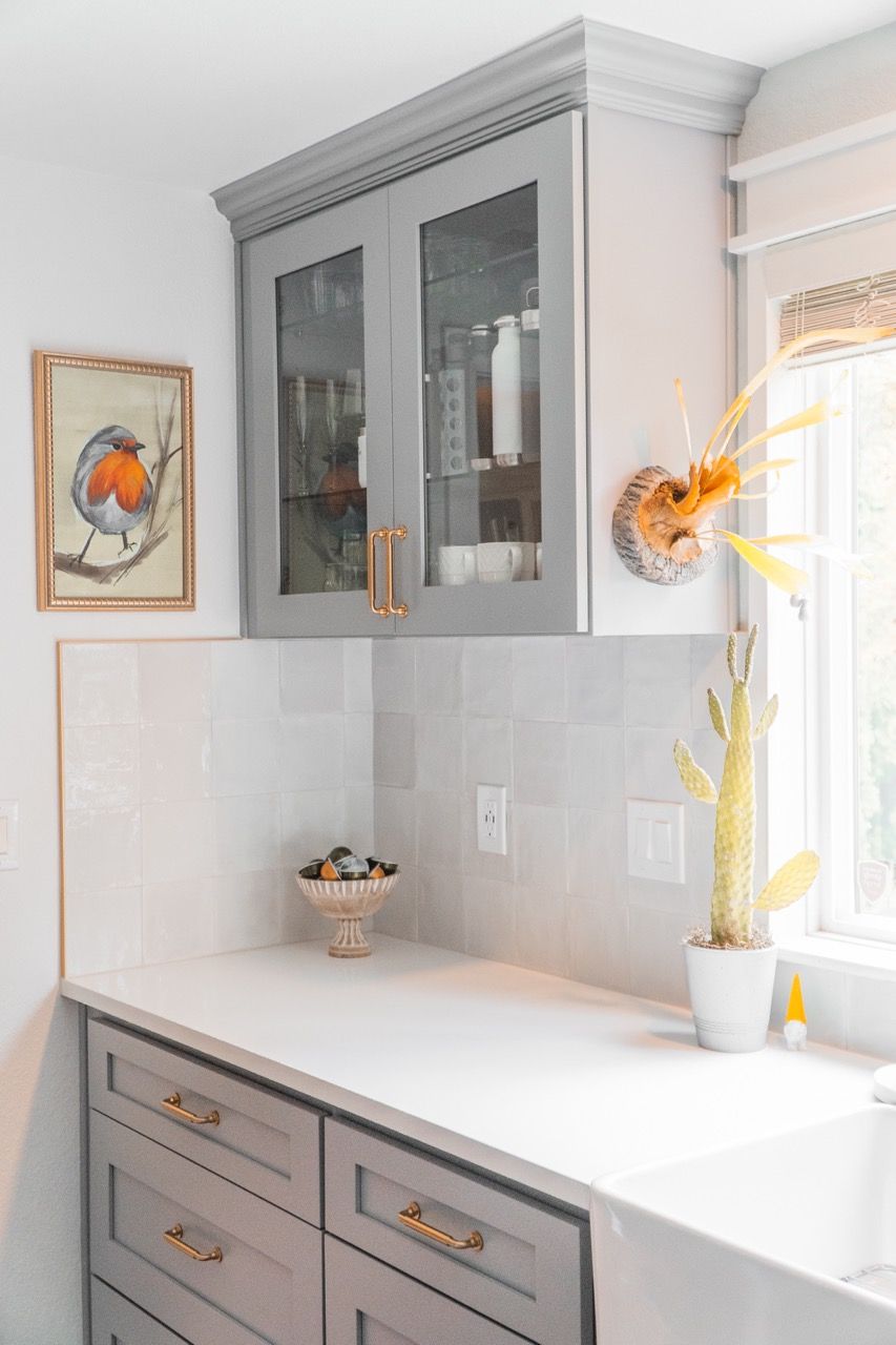 A kitchen with gray cabinets , white counter tops , and a sink.