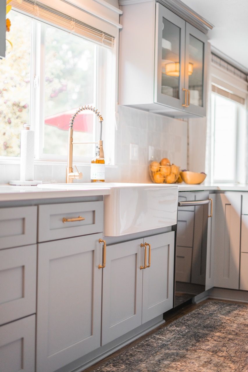 A kitchen with gray cabinets , a sink , and a window.
