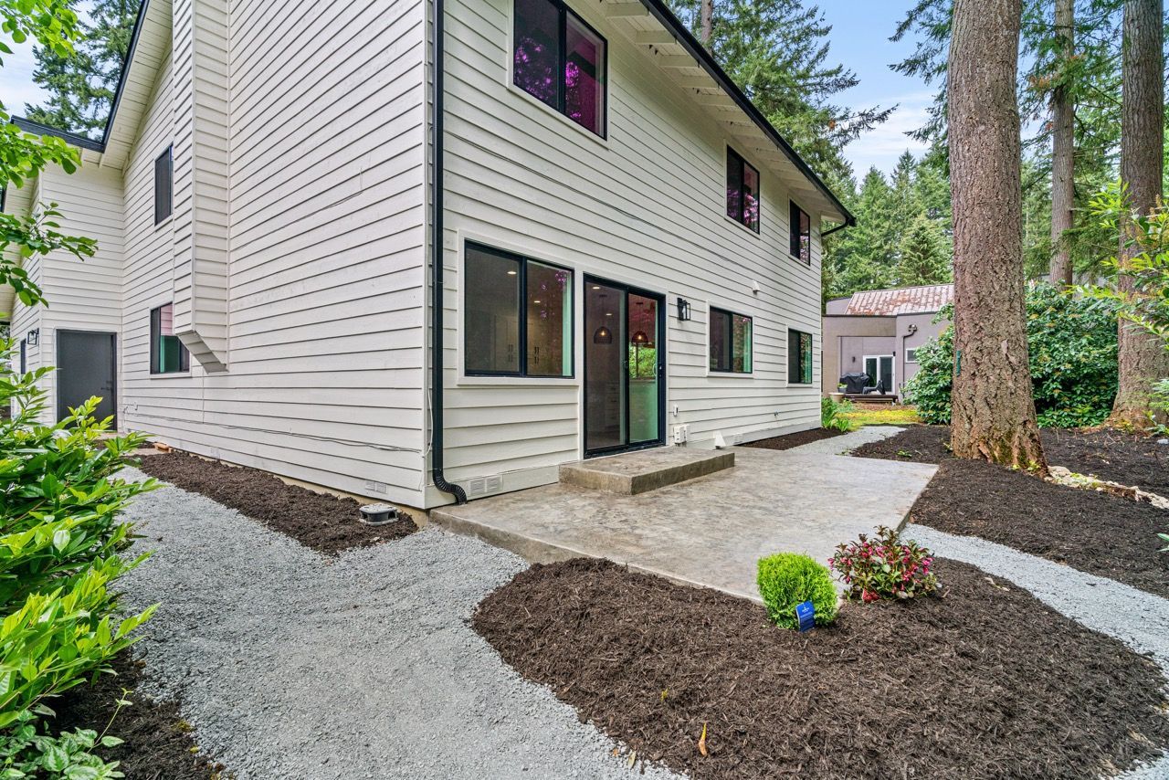 A white house with a patio in front of it is surrounded by trees.