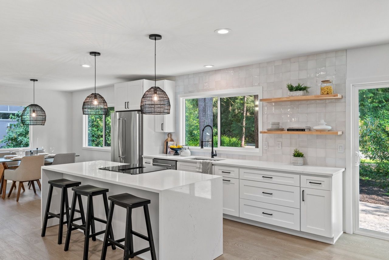 A kitchen with white cabinets , a large island , stools , a refrigerator and a stove.