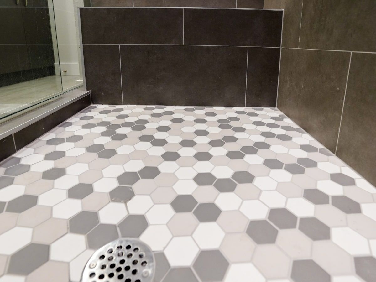 A shower stall with a hexagonal tile floor and a drain.