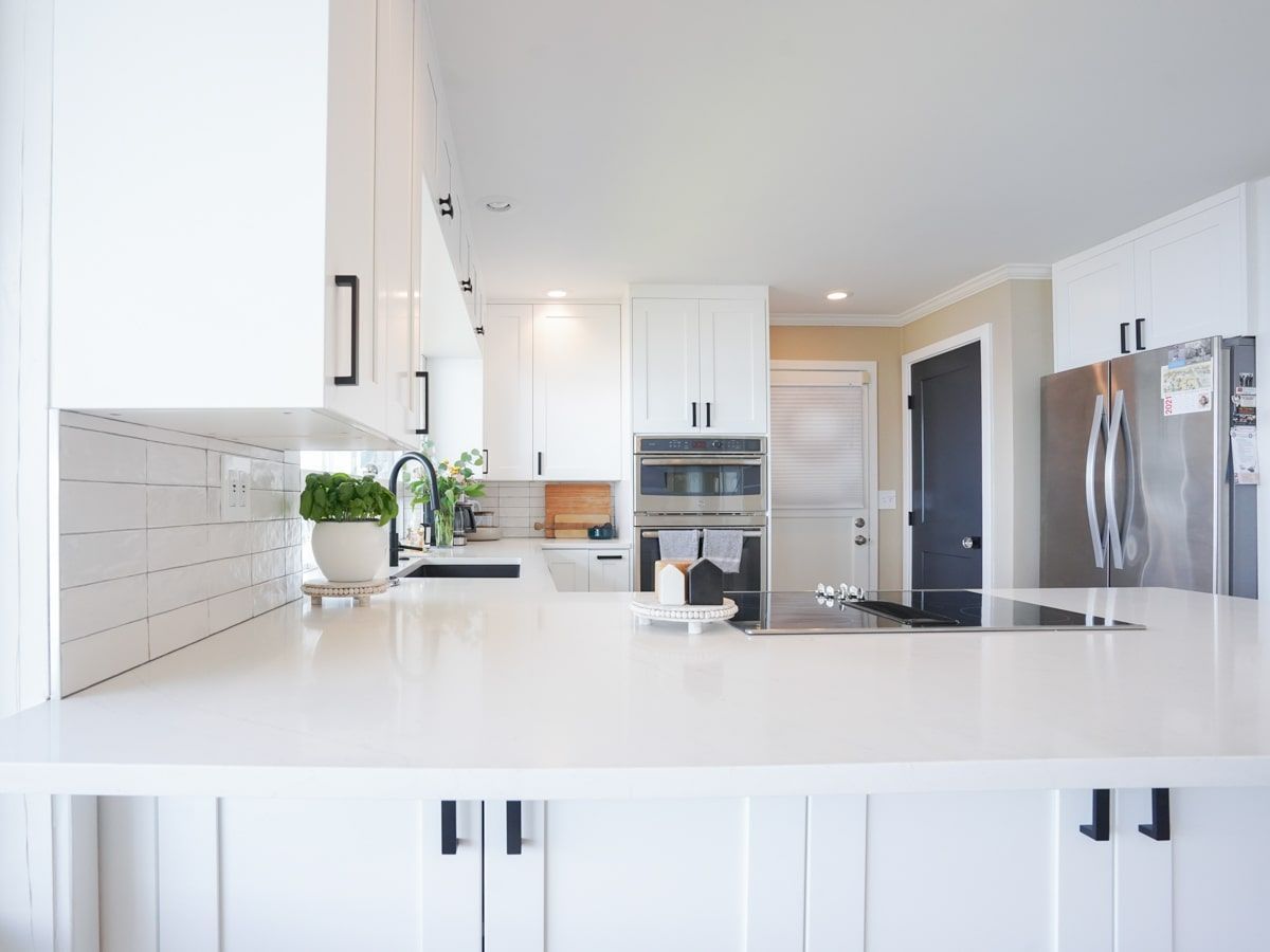 A kitchen with white cabinets , white counter tops , stainless steel appliances and a stainless steel refrigerator.