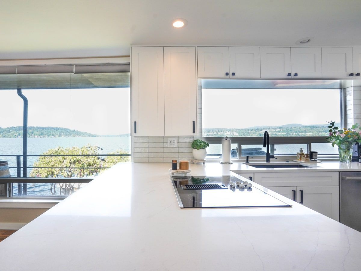 A kitchen with white cabinets and a large window overlooking the water.