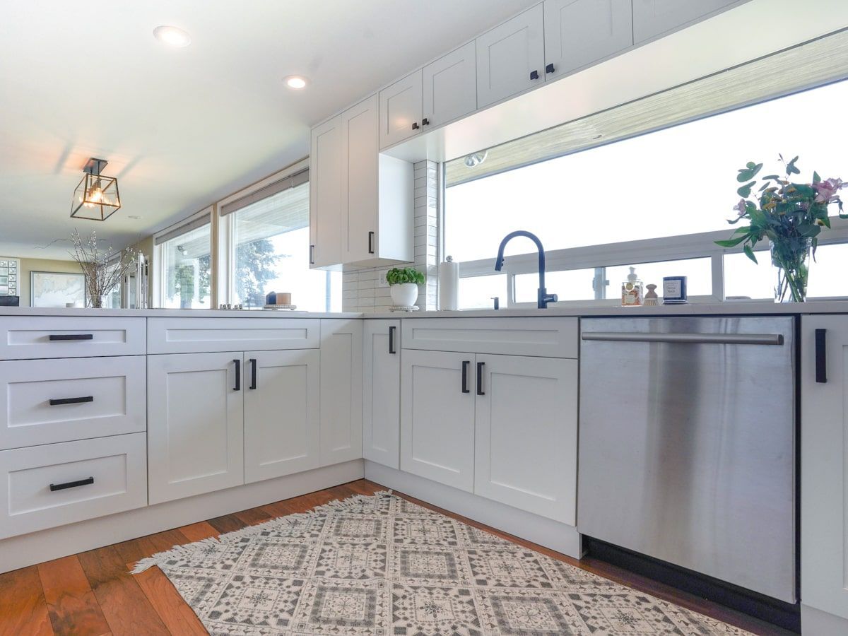 A kitchen with white cabinets , stainless steel appliances , a rug and a large window.