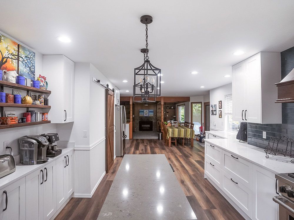 A kitchen with white cabinets , hardwood floors , and a large island.