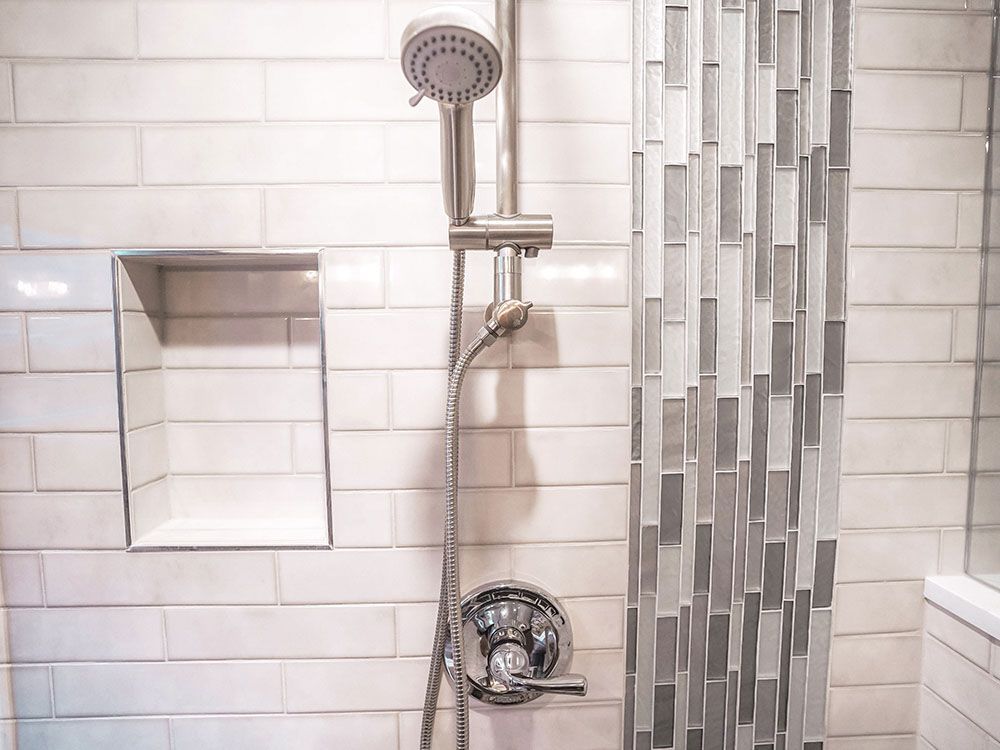A close up of a shower head in a bathroom with white tiles.