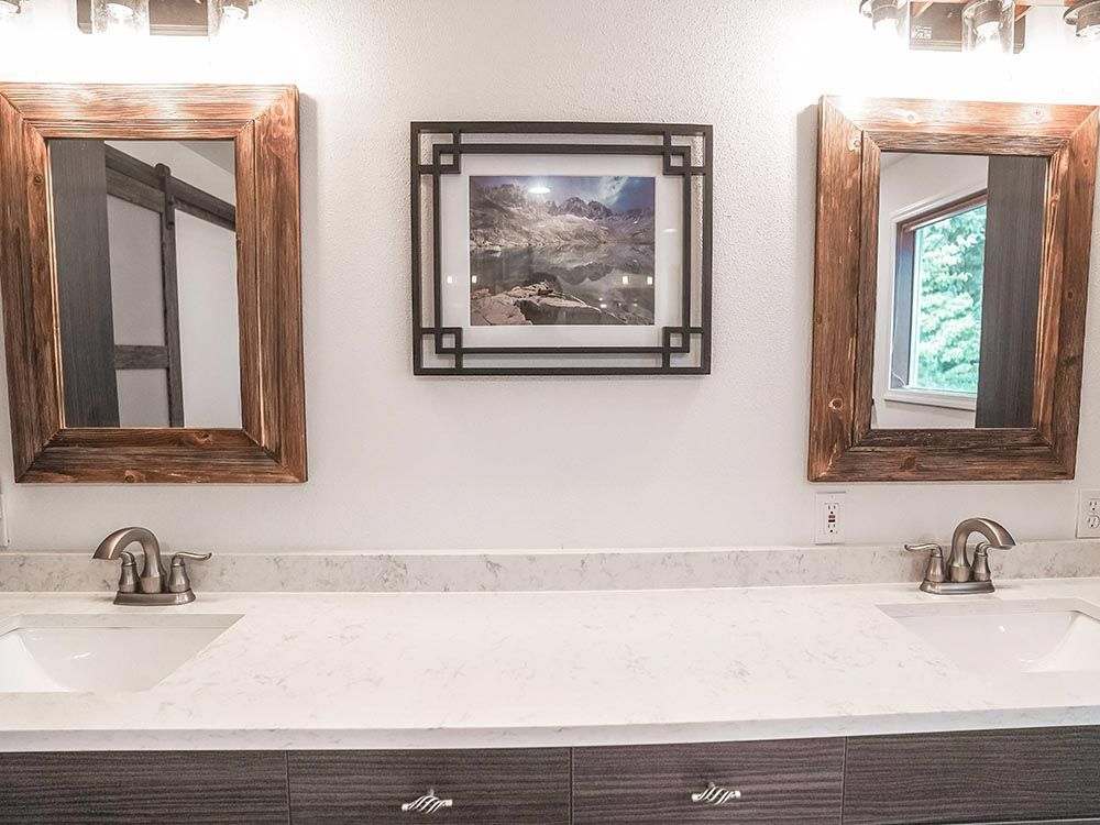 A bathroom with two sinks , two mirrors and a picture on the wall.