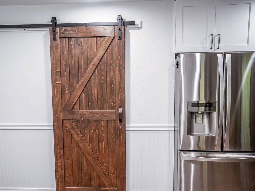 A kitchen with a sliding barn door and a stainless steel refrigerator.