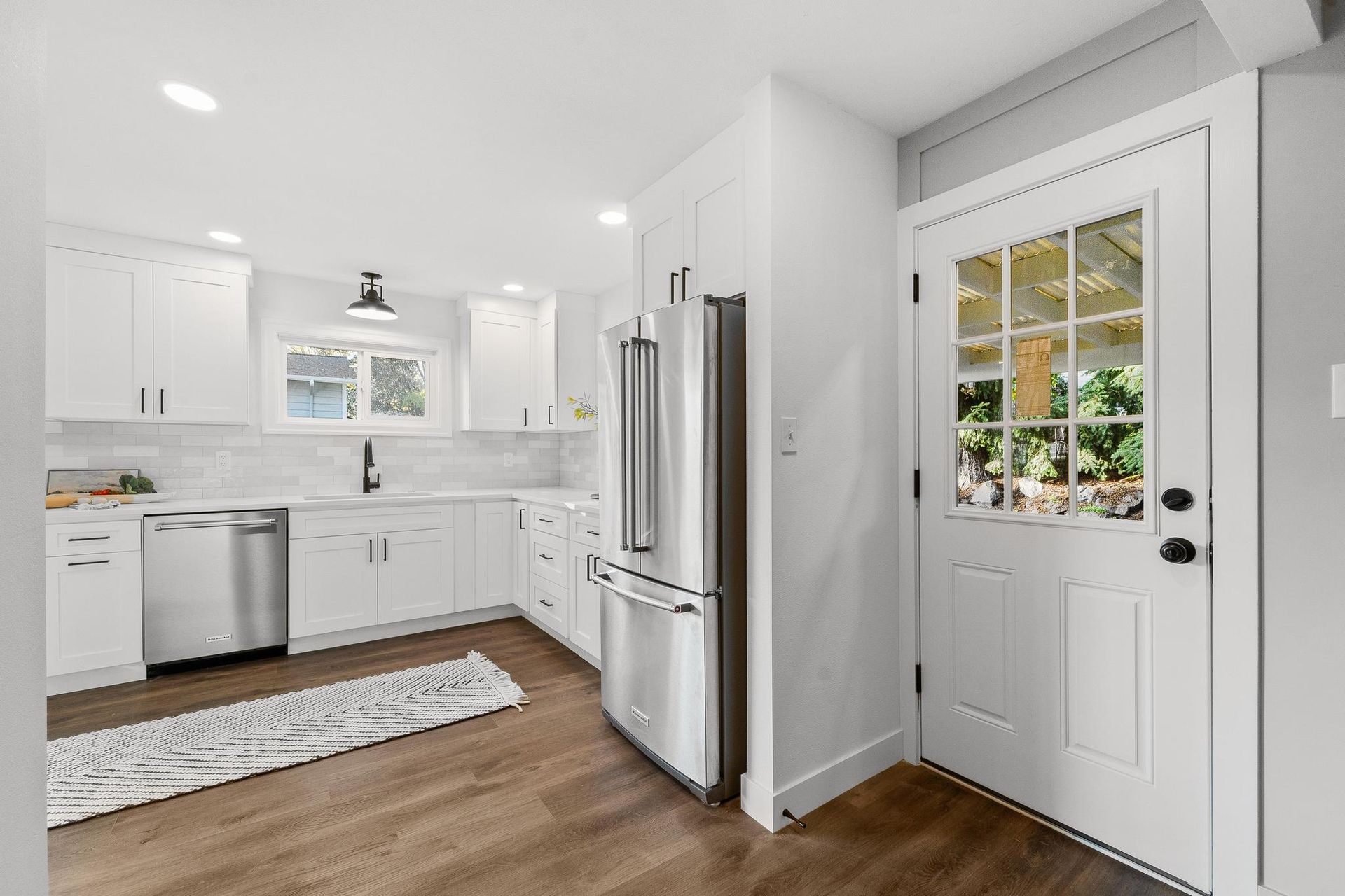 A kitchen with white cabinets , stainless steel appliances , a refrigerator and a door.
