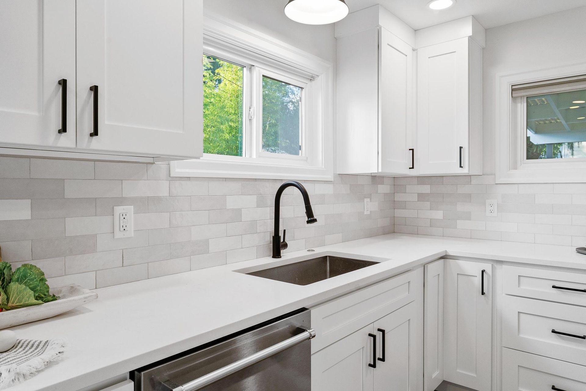 A kitchen with white cabinets , stainless steel appliances , a sink and a window.