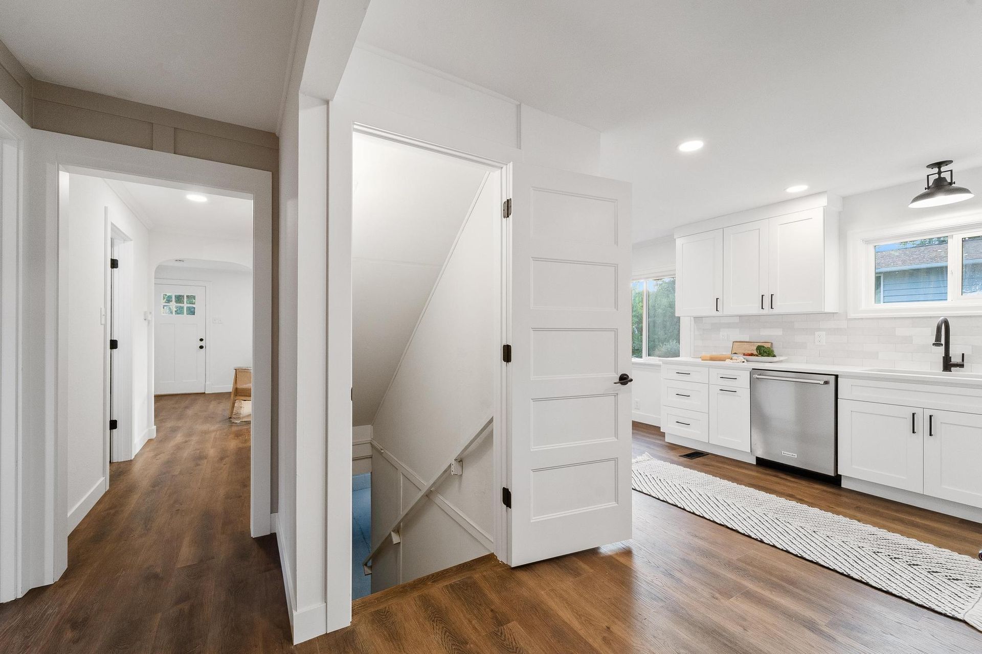 A kitchen with white cabinets and hardwood floors and a staircase leading to the second floor.