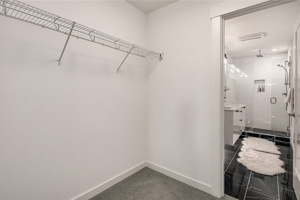 A walk in closet with a bathroom in the background.