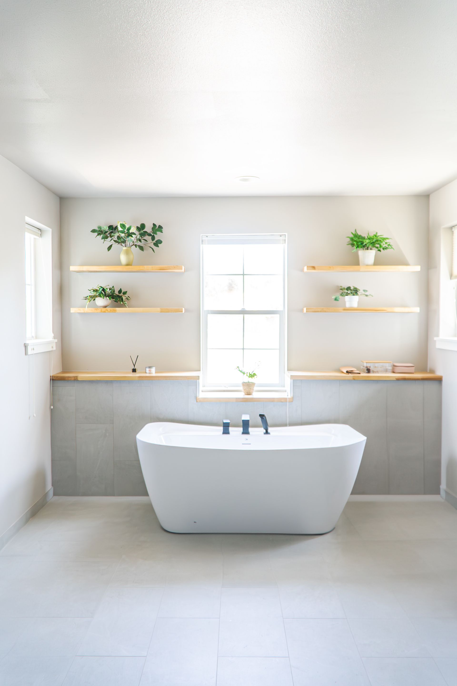 A bathroom with a tub , shelves , and a window.