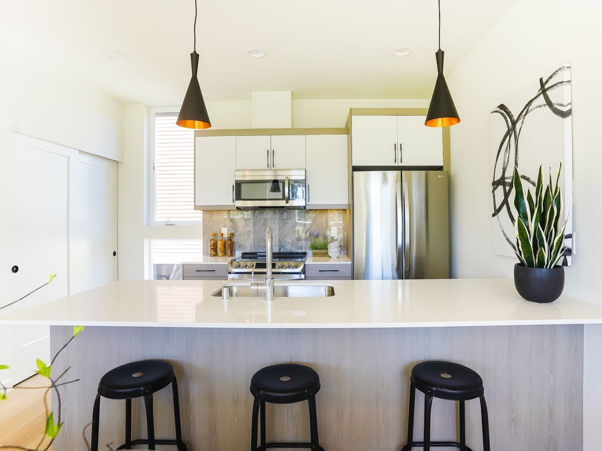 A kitchen with a stainless steel refrigerator , stove , sink , and three stools.