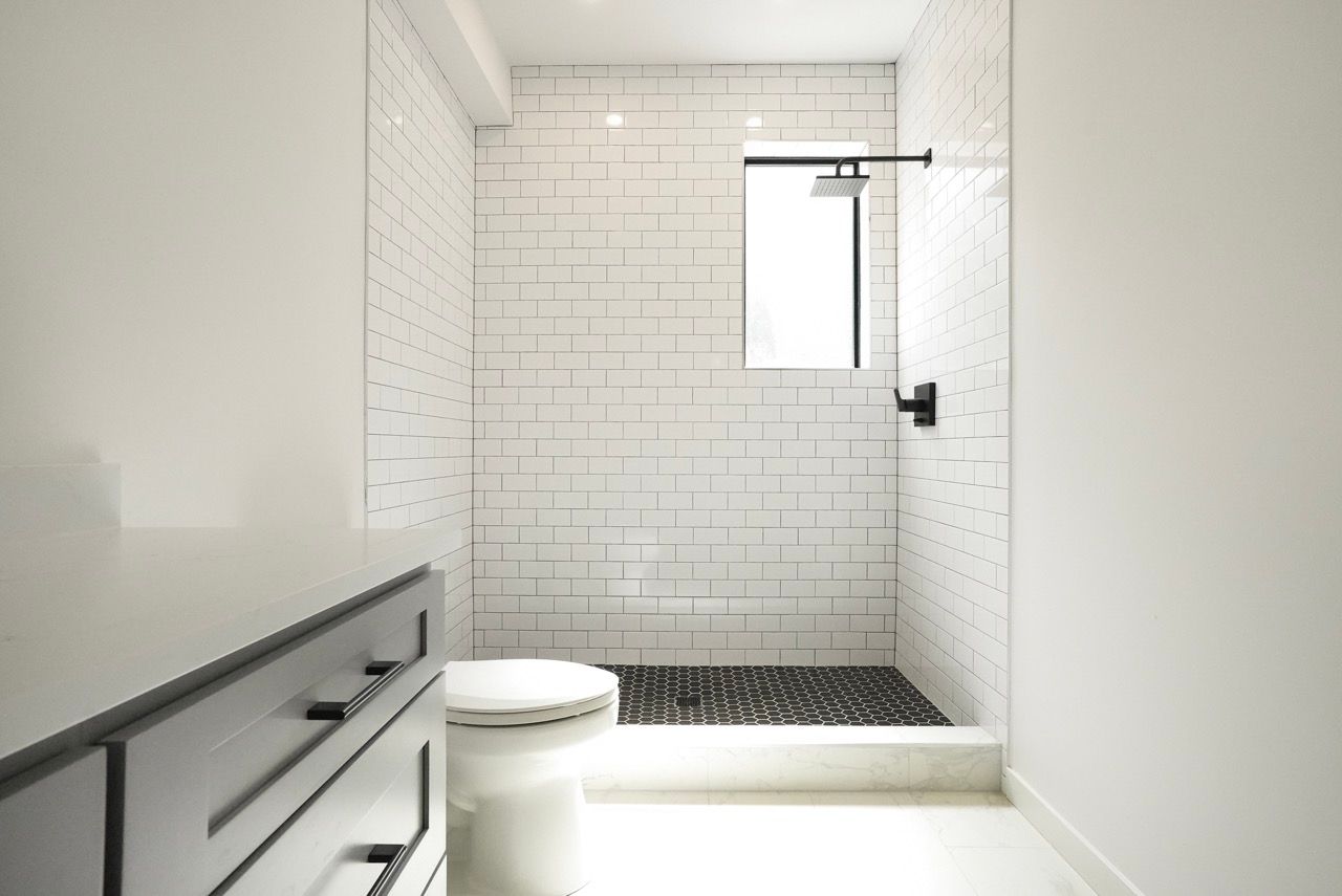 A bathroom with white tiles , a toilet , and a walk in shower.