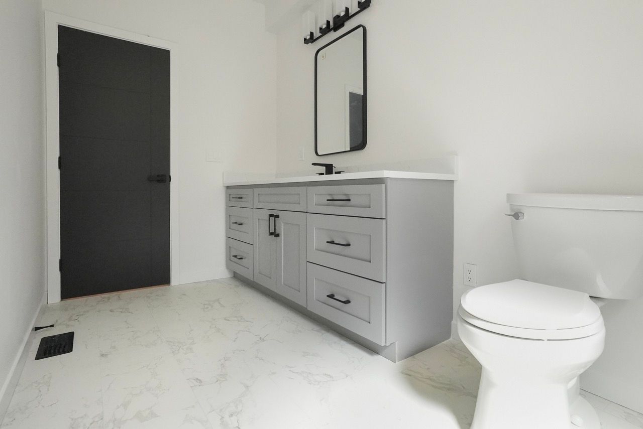 A bathroom with a toilet , sink , mirror and black door.