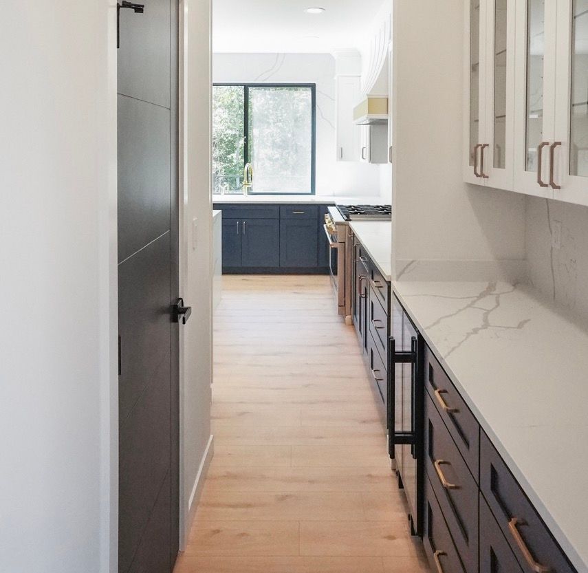 A long hallway leading to a kitchen with blue cabinets and white counter tops.