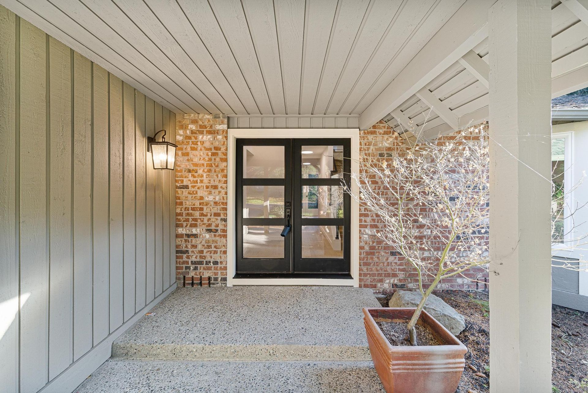 A porch with a brick wall and a black door