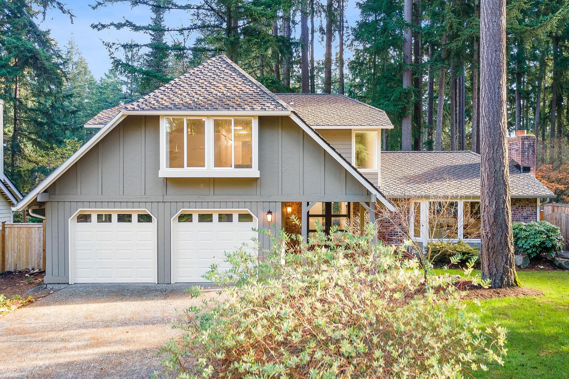 A house with two garage doors is surrounded by trees.