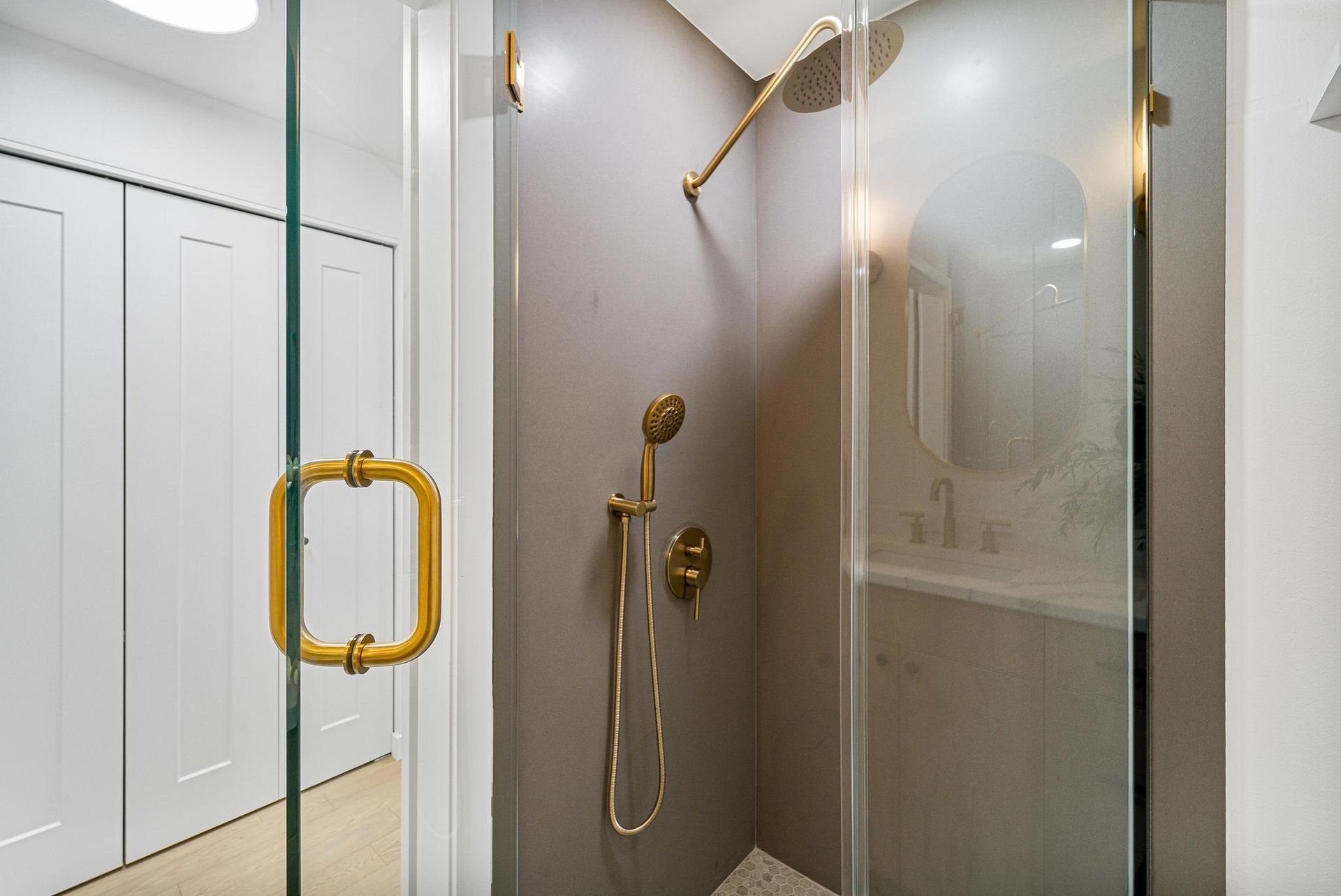 A bathroom with a walk in shower with a gold shower head.