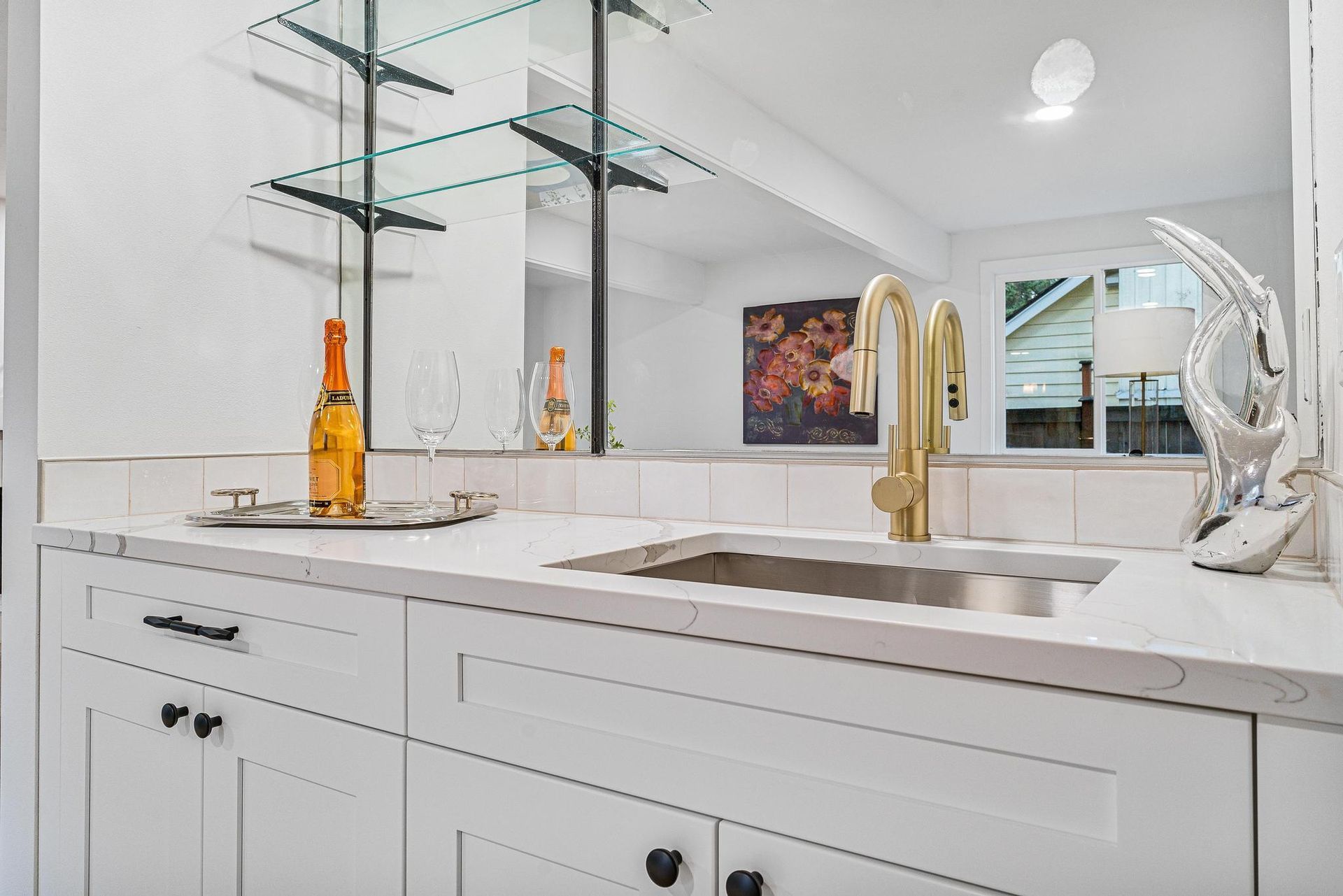 A kitchen with white cabinets , a sink and a mirror.