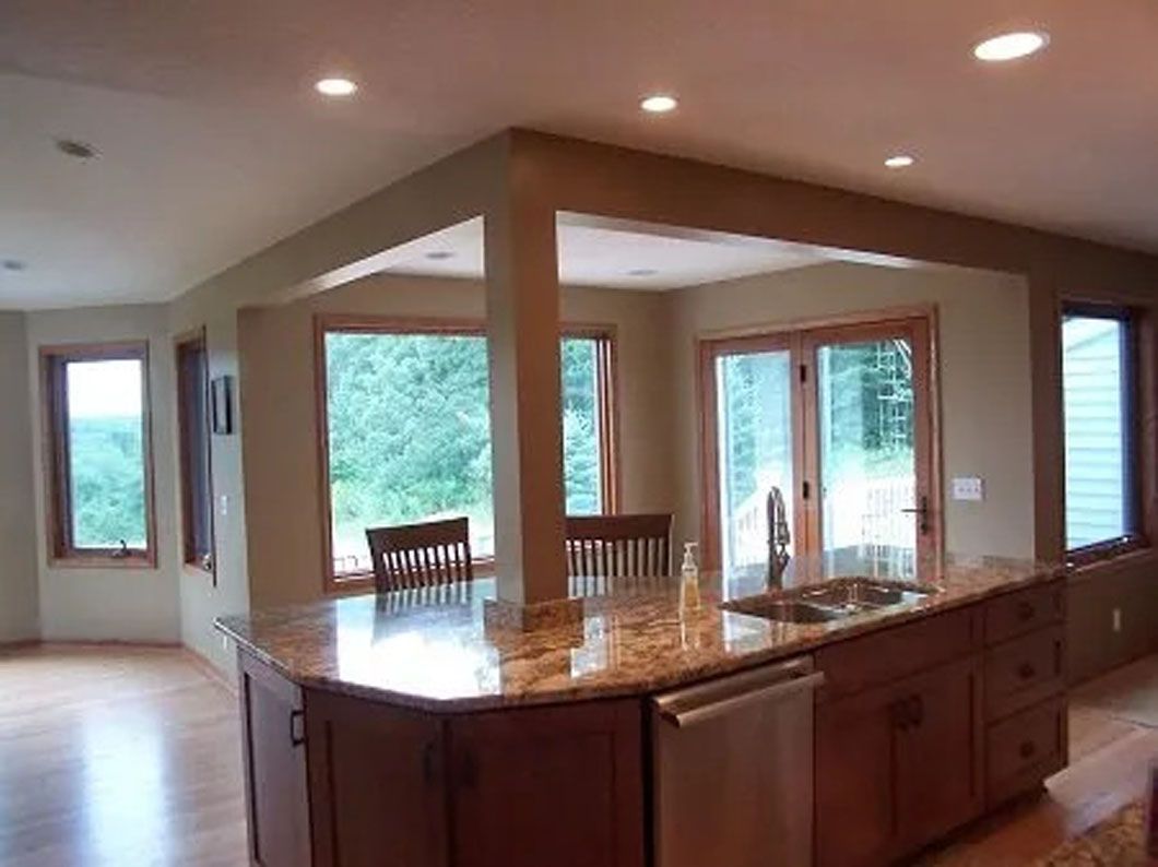Kitchen with a brown granite countertop island, cabinets, and windows overlooking nature.