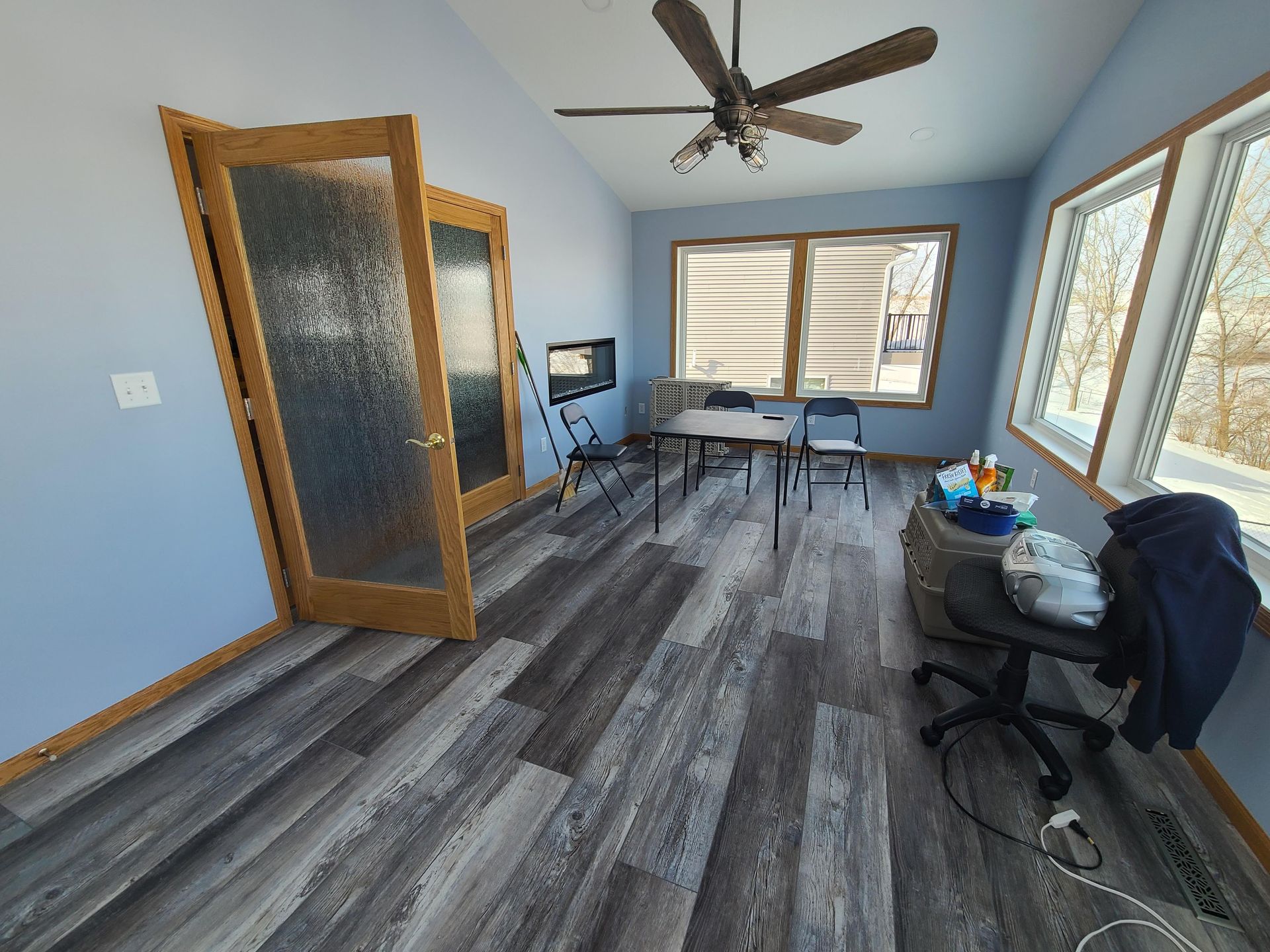 Blue-walled room with wood-look flooring. Includes doors, a table with chairs, a window, and a ceiling fan.