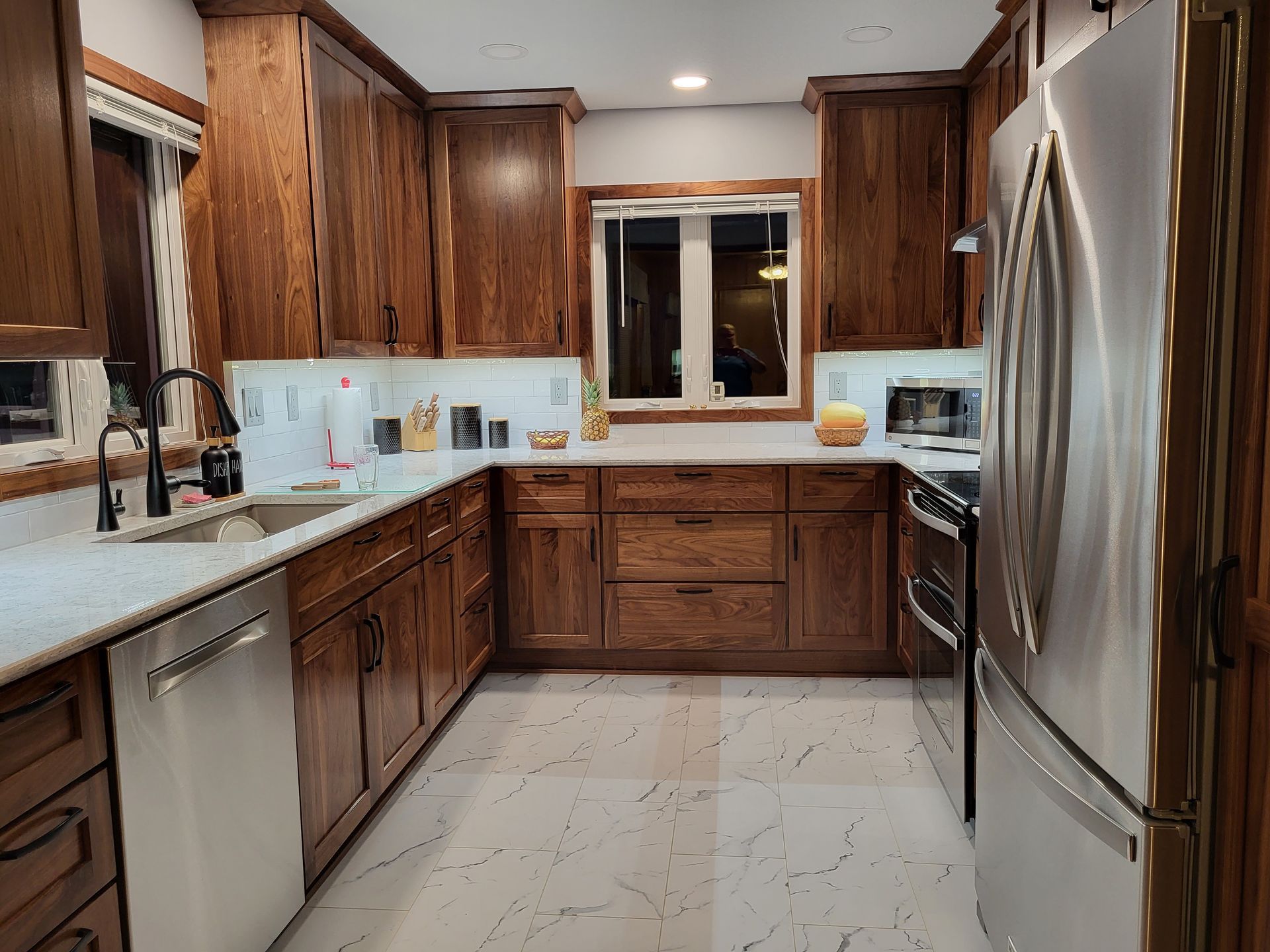 Kitchen with dark wood cabinets, stainless steel appliances, white countertops and speckled floor.