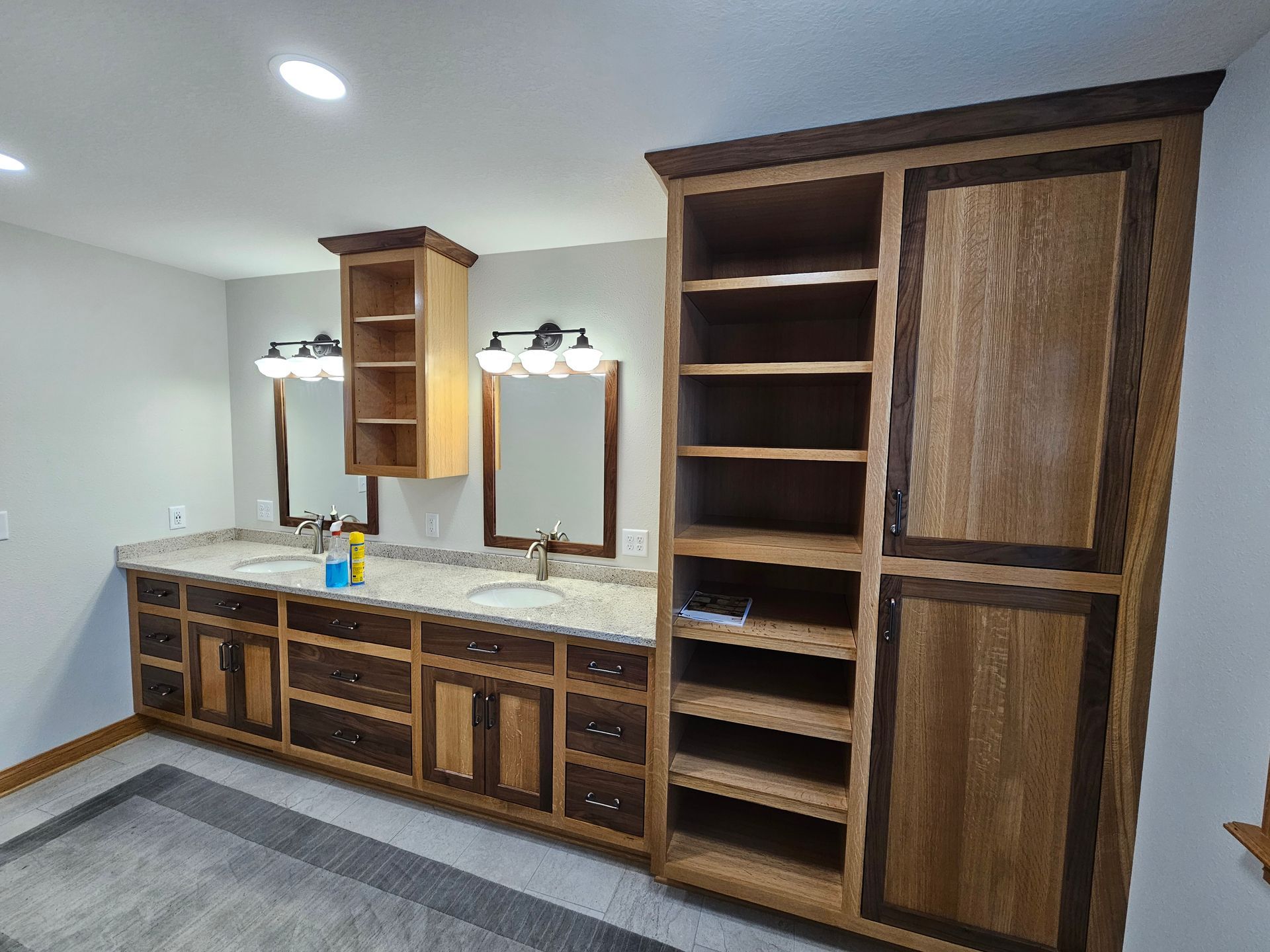 Bathroom with light-colored walls, vanity with granite countertop, and tall storage cabinet; wood tones and two sinks.