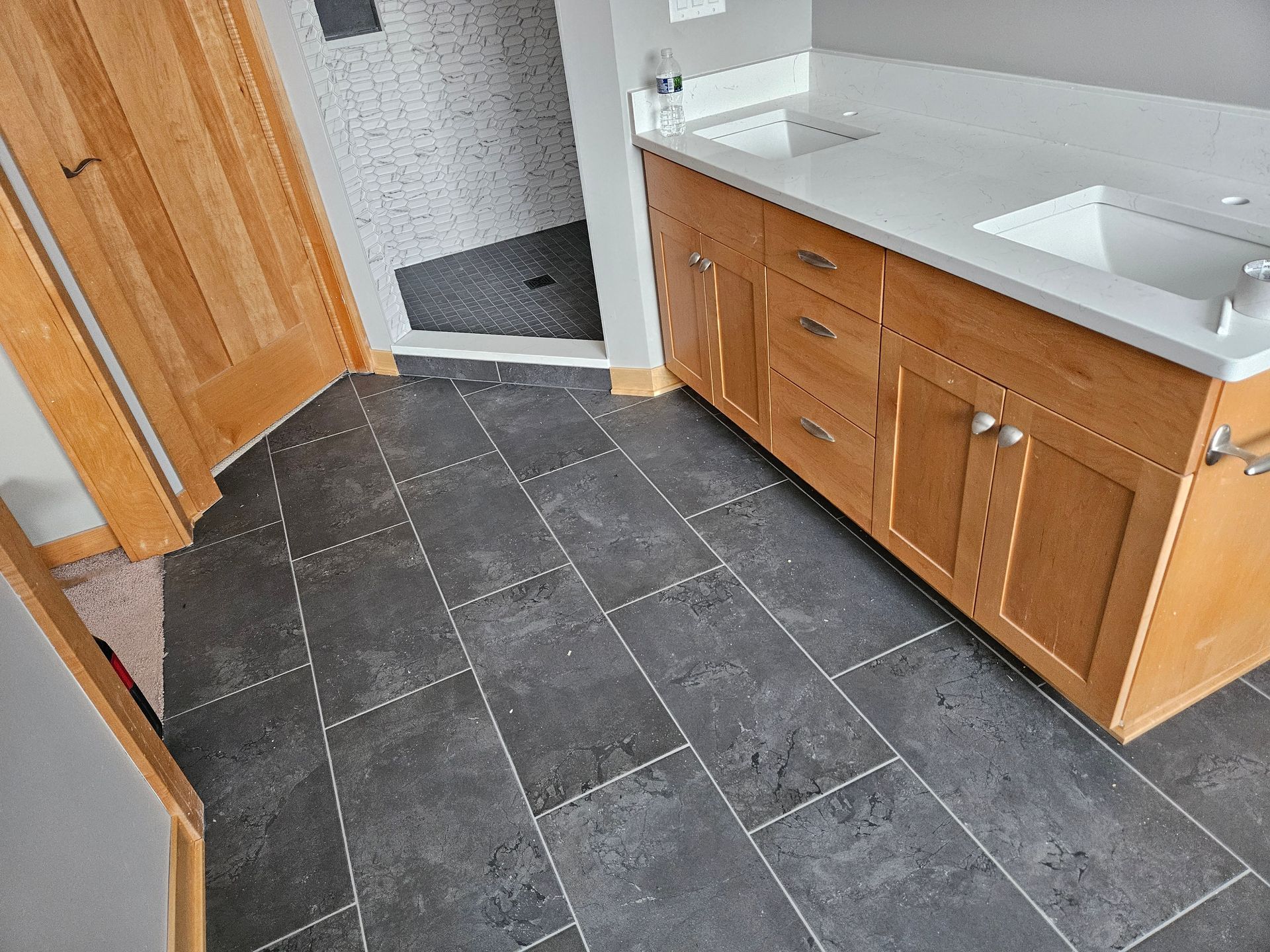 Bathroom with gray tile floor, light wood vanity, and shower with white and black tiles.