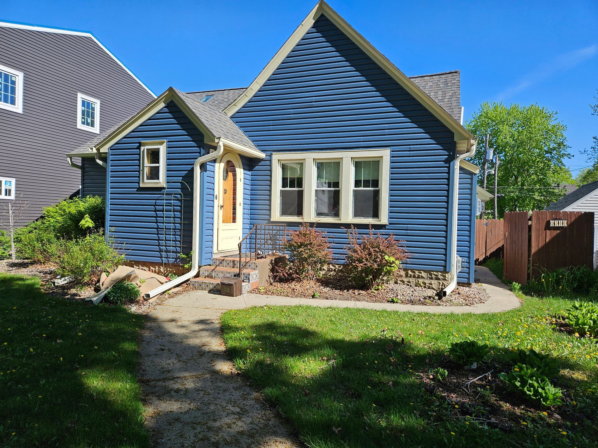 Blue cottage with gray roof, walkway, small yard, sunny day.