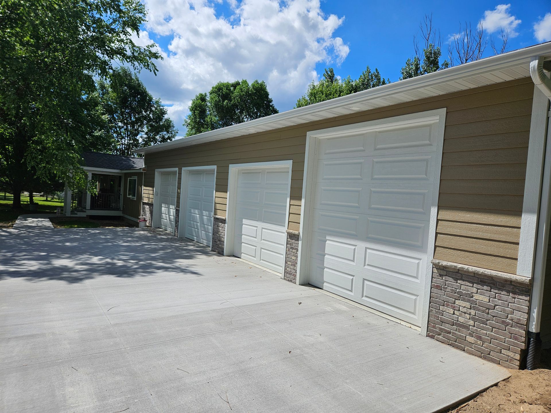 Exterior of a tan and white garage with three doors and a concrete driveway on a sunny day.