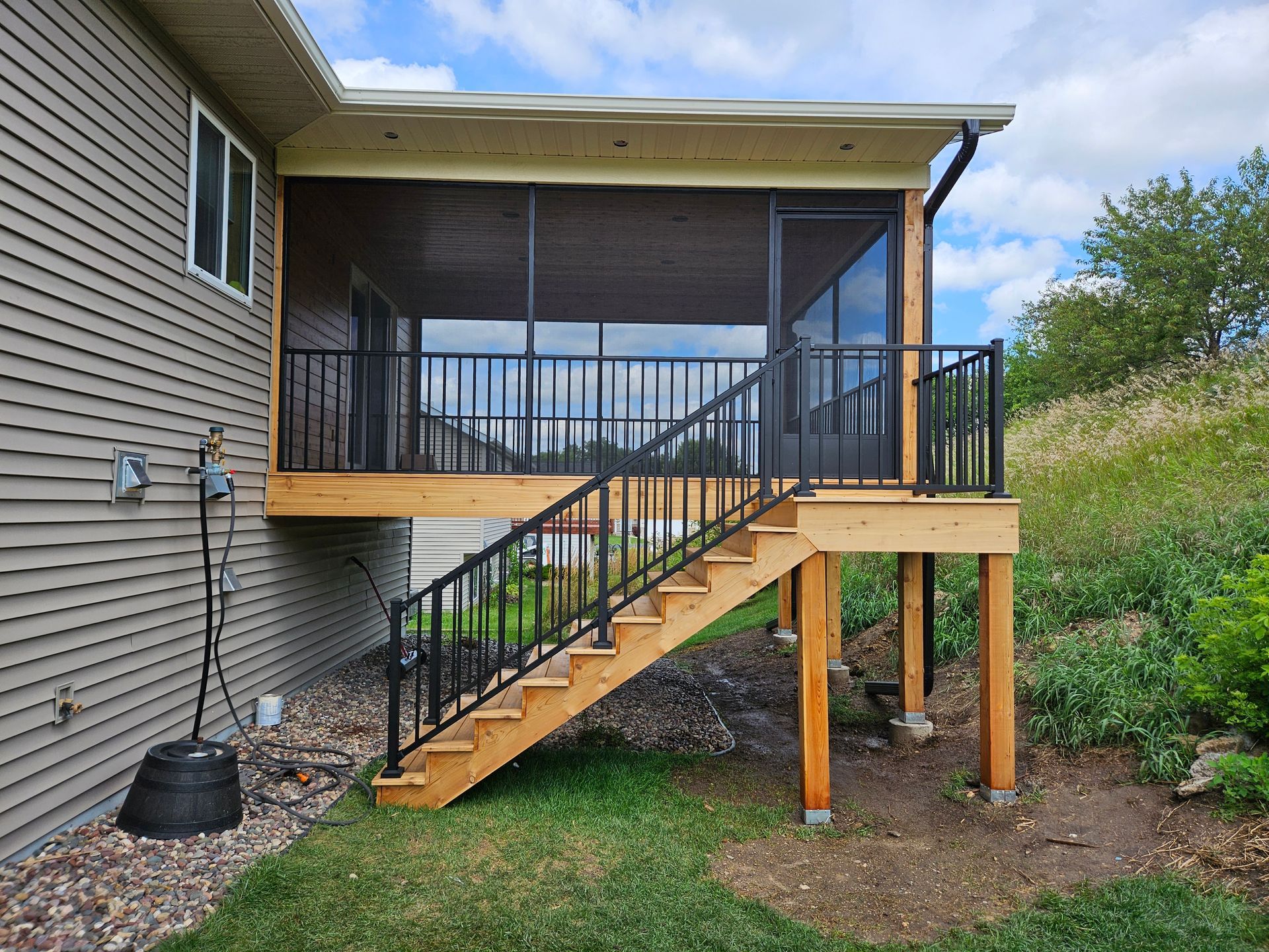 Screened porch with black railings and stairs leading down to a yard.