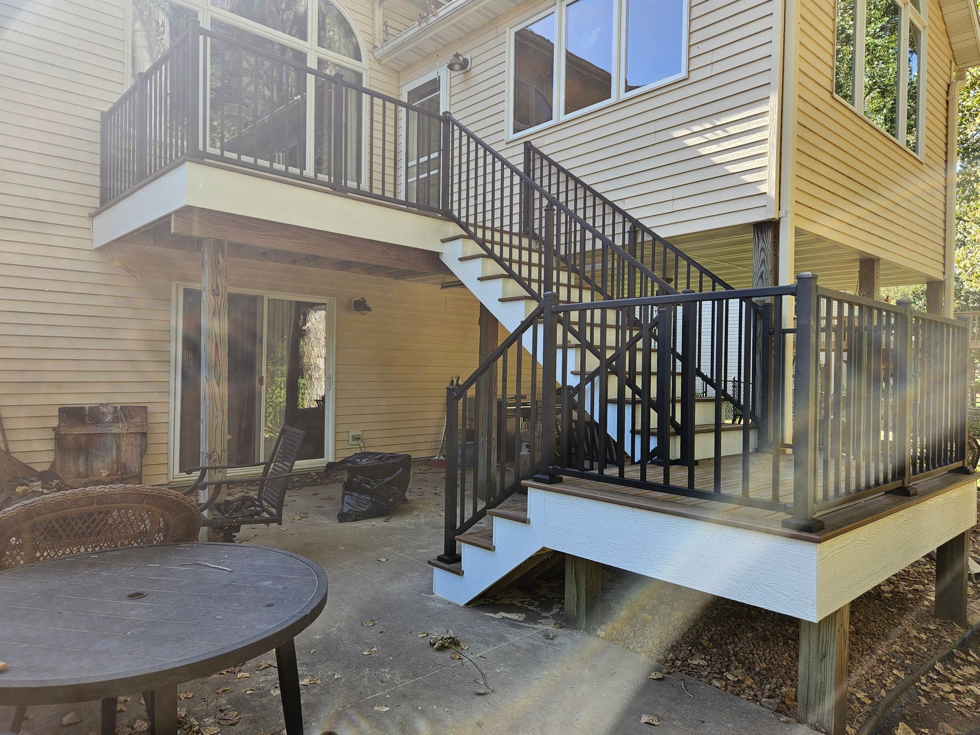 Black railing deck and stairs on a two-story house with a concrete patio.