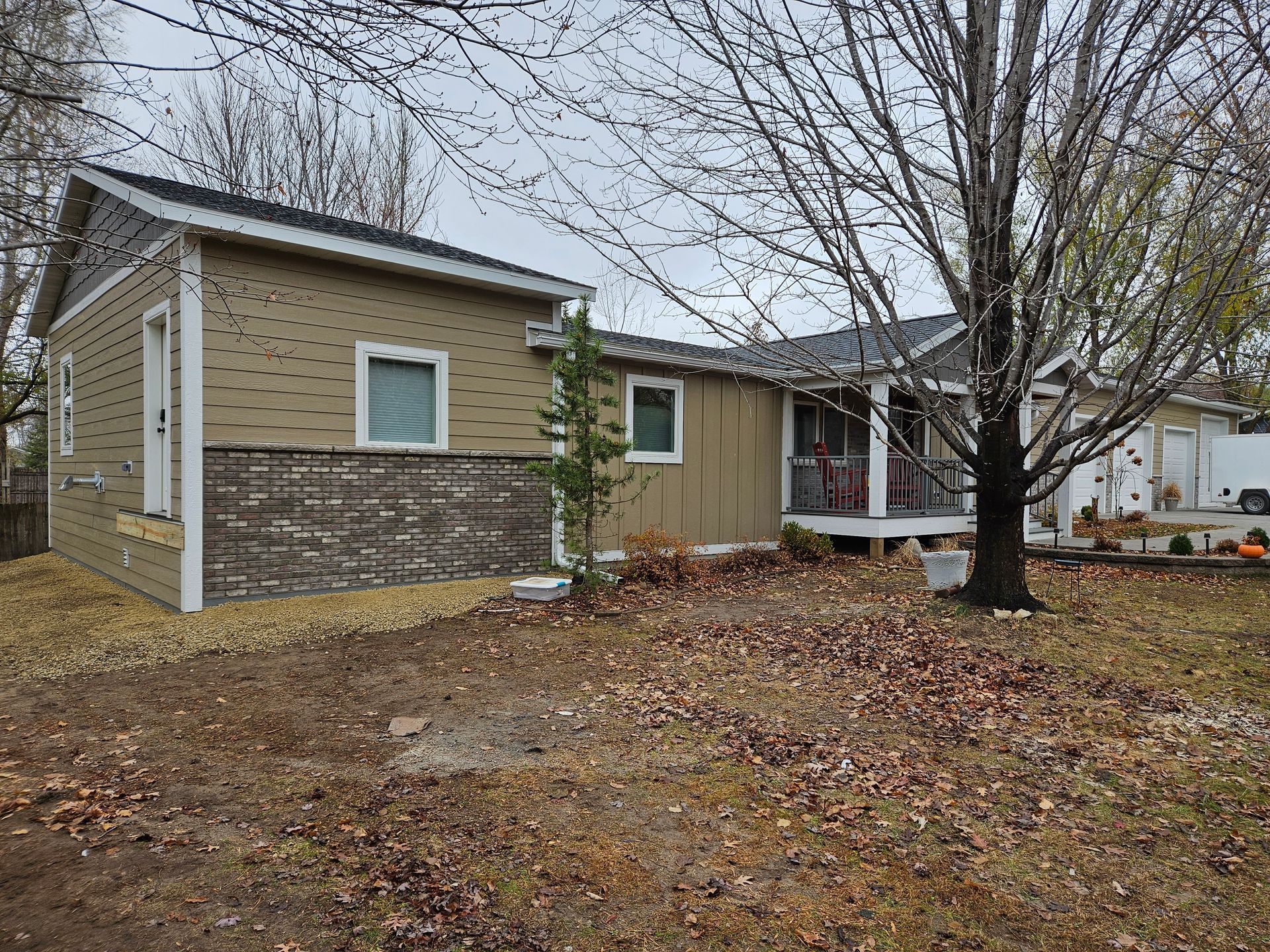 Tan and brown house under construction with a porch and bare trees.