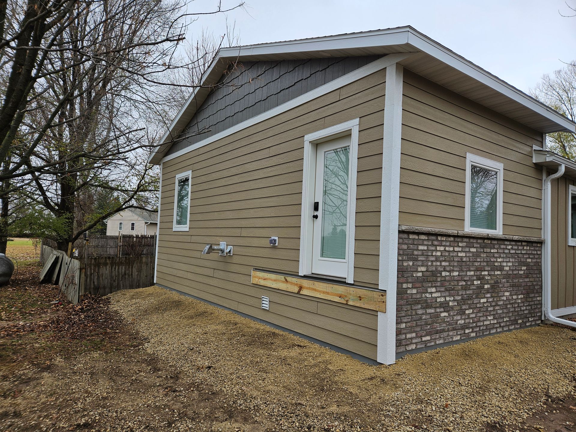 Tan house with brick base, side door, and small wooden porch.
