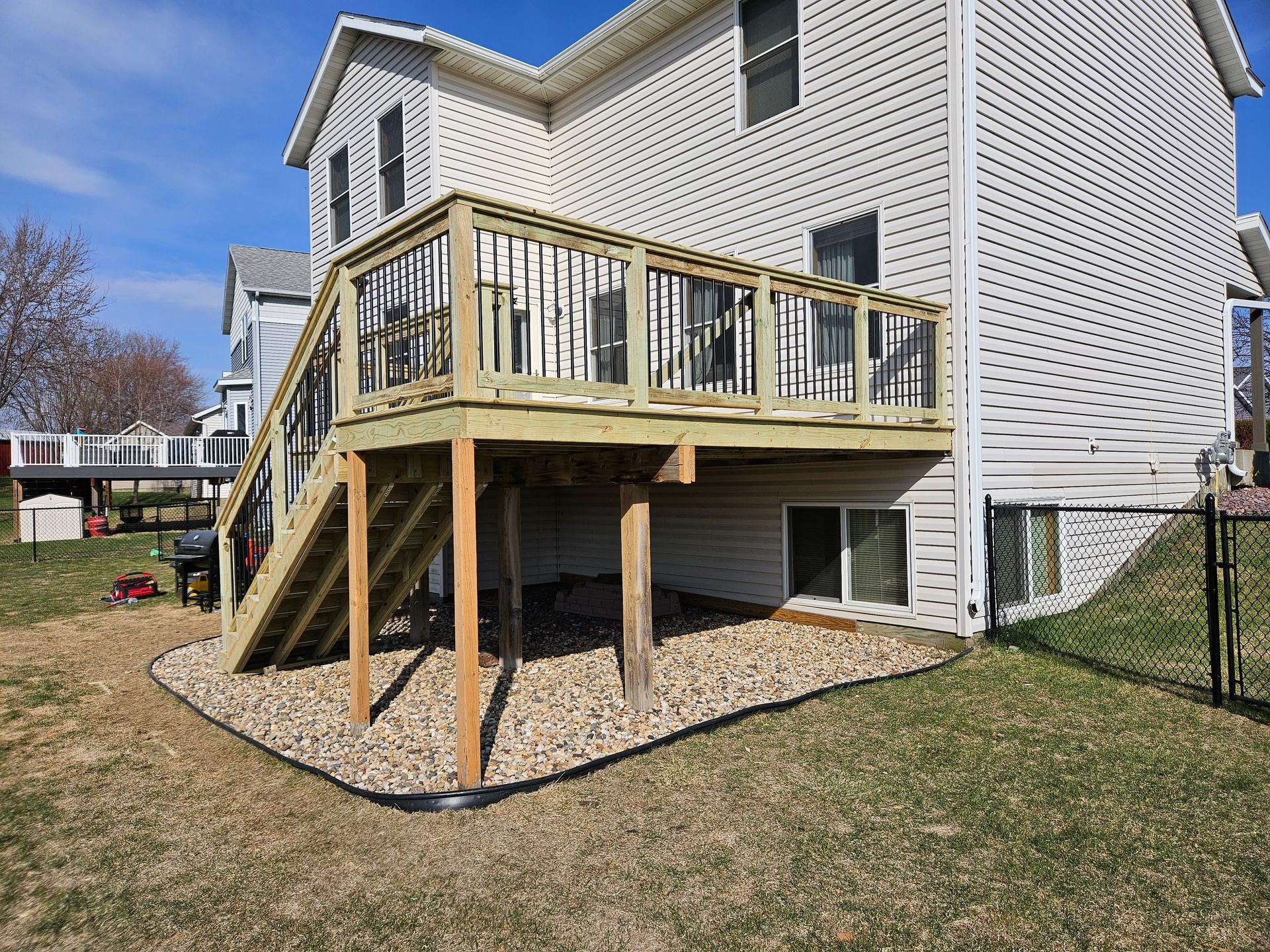 Wooden deck attached to a two-story house, with stairs and a gravel bed border in a yard.