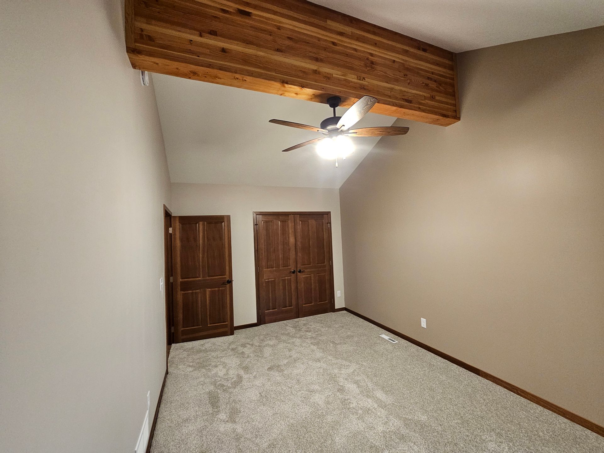 Bedroom with vaulted ceiling, wooden beams, closet doors, and neutral carpet.