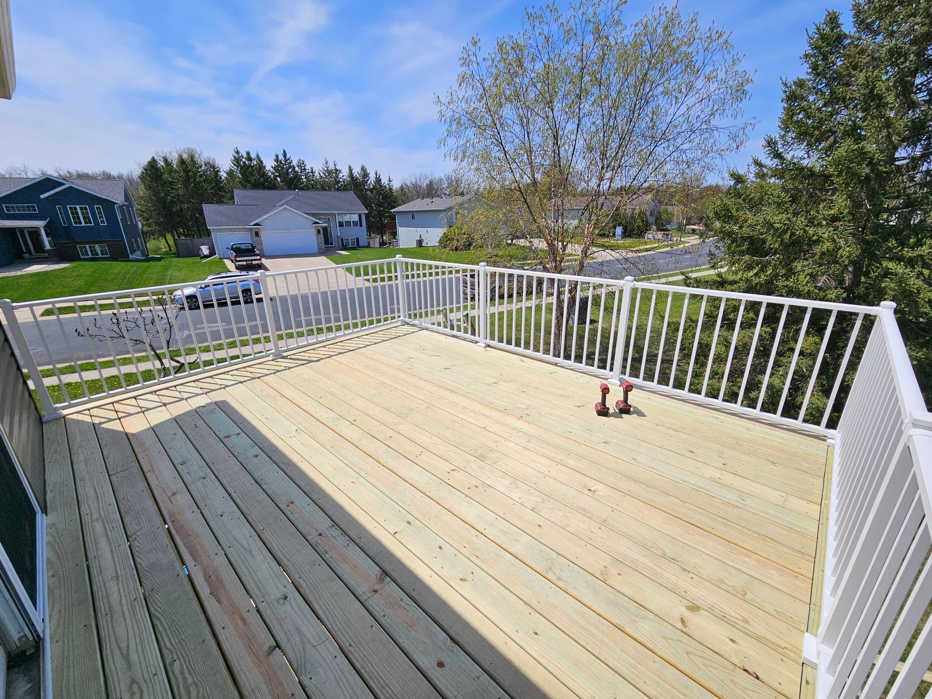 Newly built wooden deck with white railings, overlooking a residential neighborhood on a sunny day.