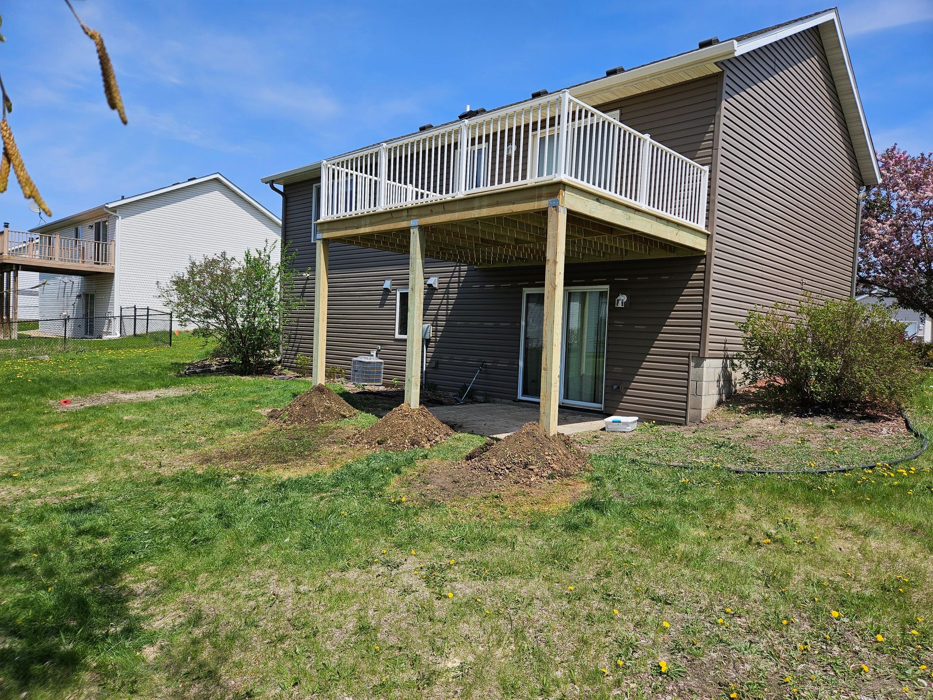 A two-story house with a wooden deck, brown siding, and grassy yard.