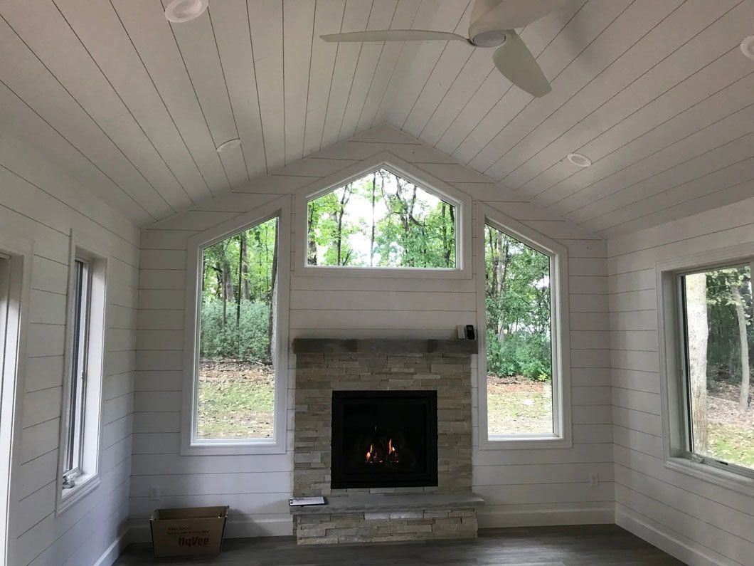White-walled room with fireplace, windows, and a vaulted ceiling with a ceiling fan; view to the outdoors.