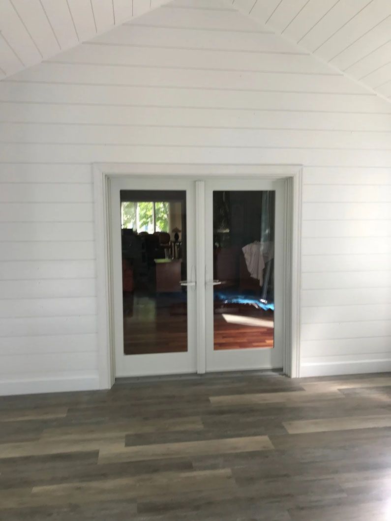 White paneled room with French doors. Gray wood-look floor.