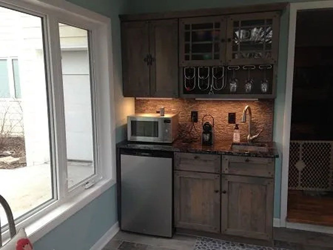 Small kitchen area with cabinets, a sink, mini fridge, microwave, and wine glasses.