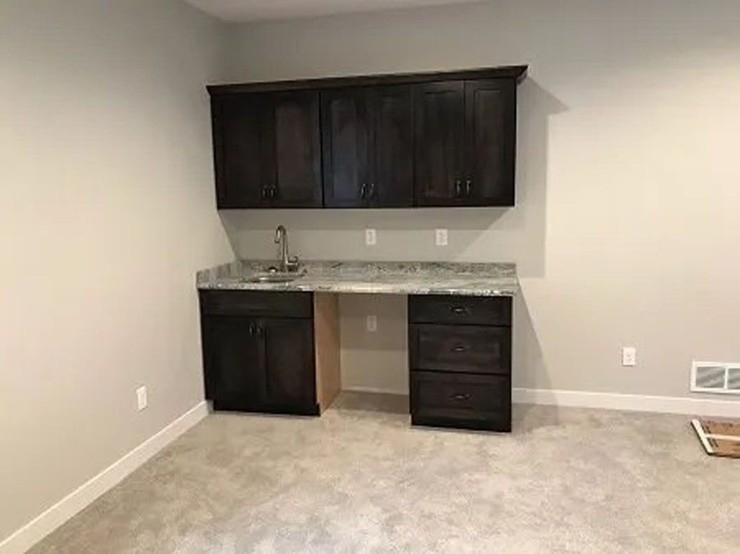 Dark wood cabinets with sink and granite countertop in a room with light walls and flooring.