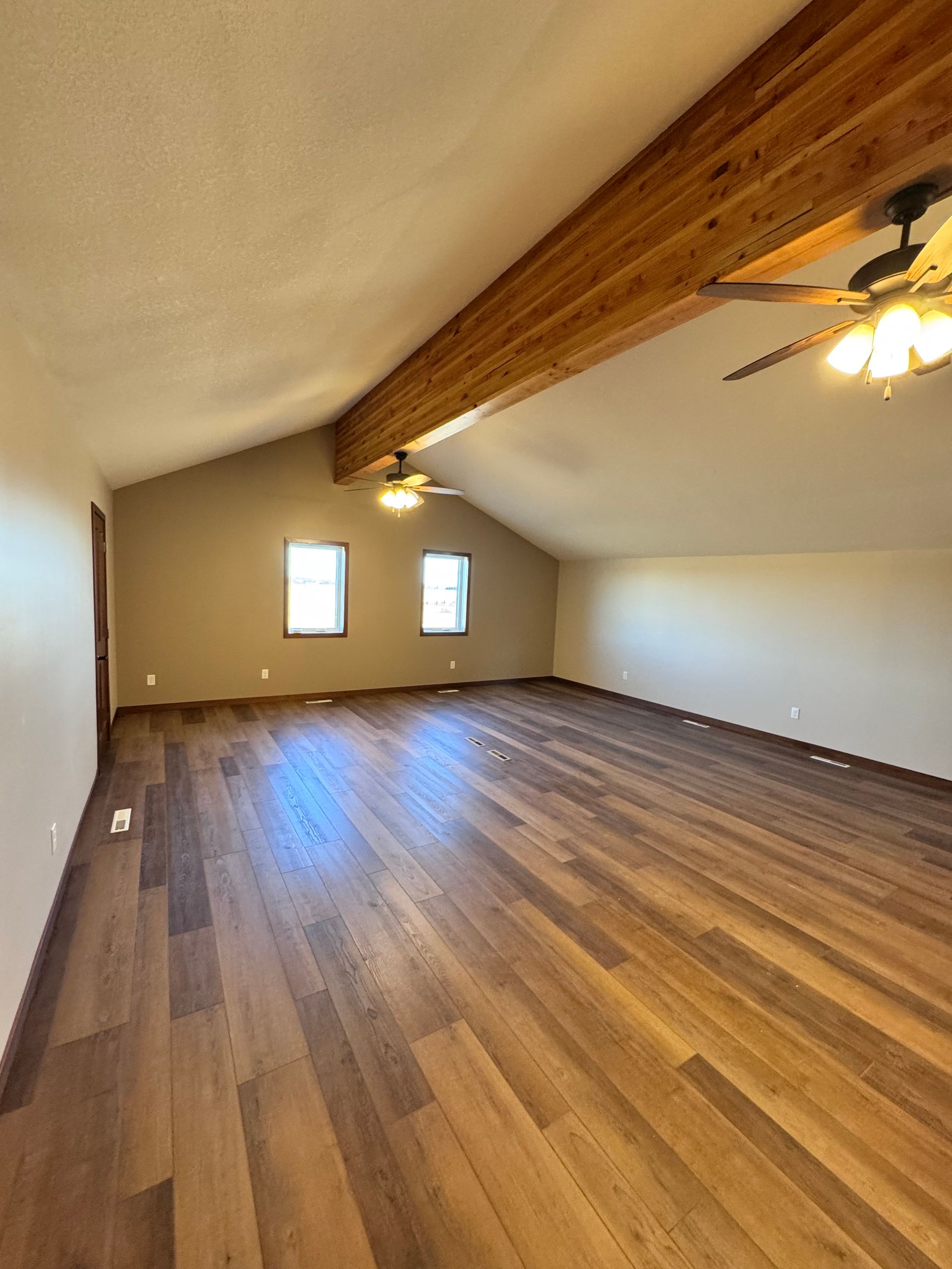 Spacious room with wood floors, exposed beam ceiling, and two windows on the far wall.