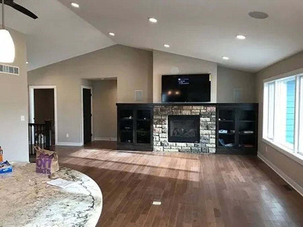 Living room with fireplace, TV, and dark cabinets. Hardwood floors and beige walls.