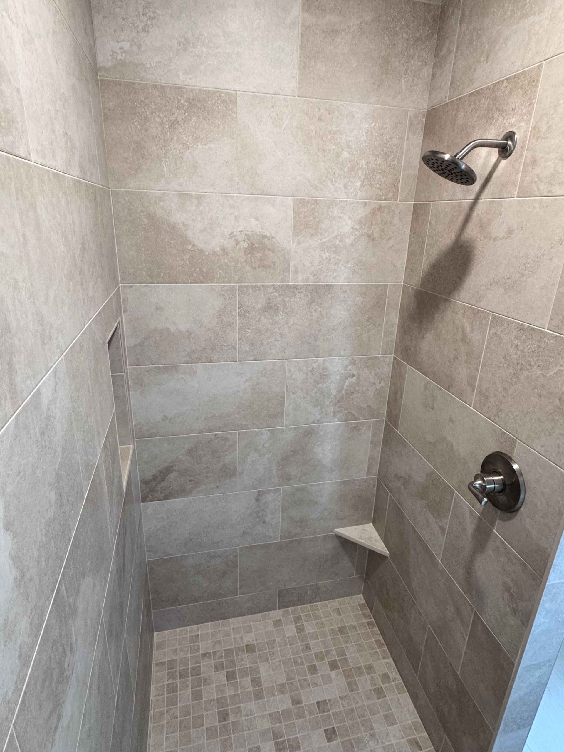 Shower stall with beige tile, a shower head, and a built-in bench.
