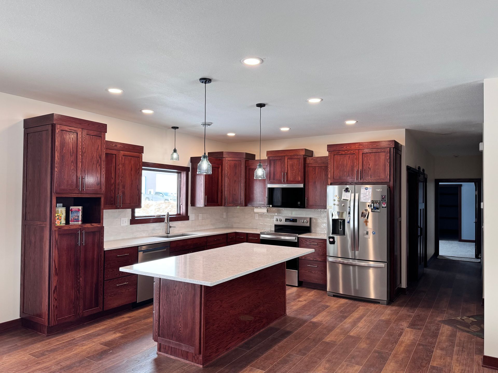 Red-toned kitchen with island, cabinets, and stainless steel appliances on wood floor.